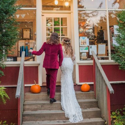 Bride and groom climb porch steps past jack-o'-lanterns toward a lit doorway of the lodge