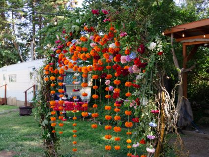 Floral arch covered in marigold garlands and roses stands in front of a vintage trailer