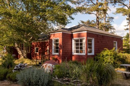 Red shingled cabin exterior surrounded by trees and garden plantings