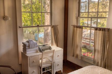Lodge suite desk with vintage typewriter and folded towels between two curtained windows