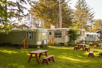 Row of renovated vintage trailers on a lawn with red picnic tables set up between them