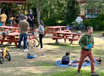 People, kids and dogs gathered around picnic tables on the lawn near the African Queen trailer