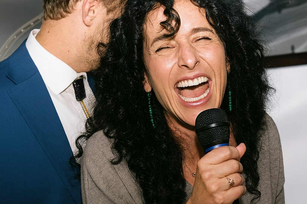 Woman with curly hair laughing and singing into a microphone at a party