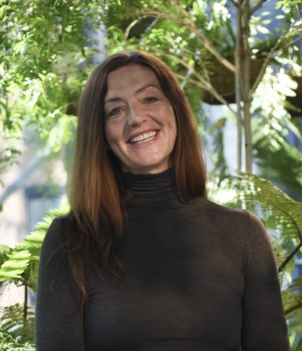Portrait of artist Meaghan Lynch smiling outdoors among ferns and greenery