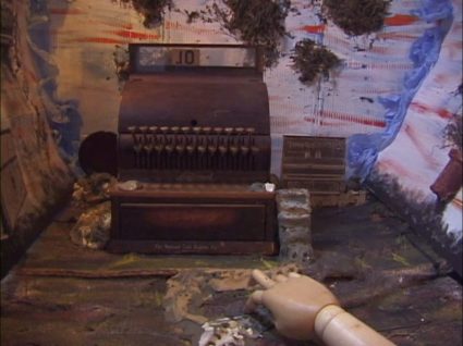 Another frame of the antique cash register stop motion set with a hand reaching toward it