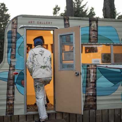 A vintage trailer painted with a blue wave mural and the words Art Gallery above its open door