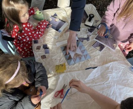 Children and an adult cut and arrange triangle fabric patches on a paper covered outdoor table
