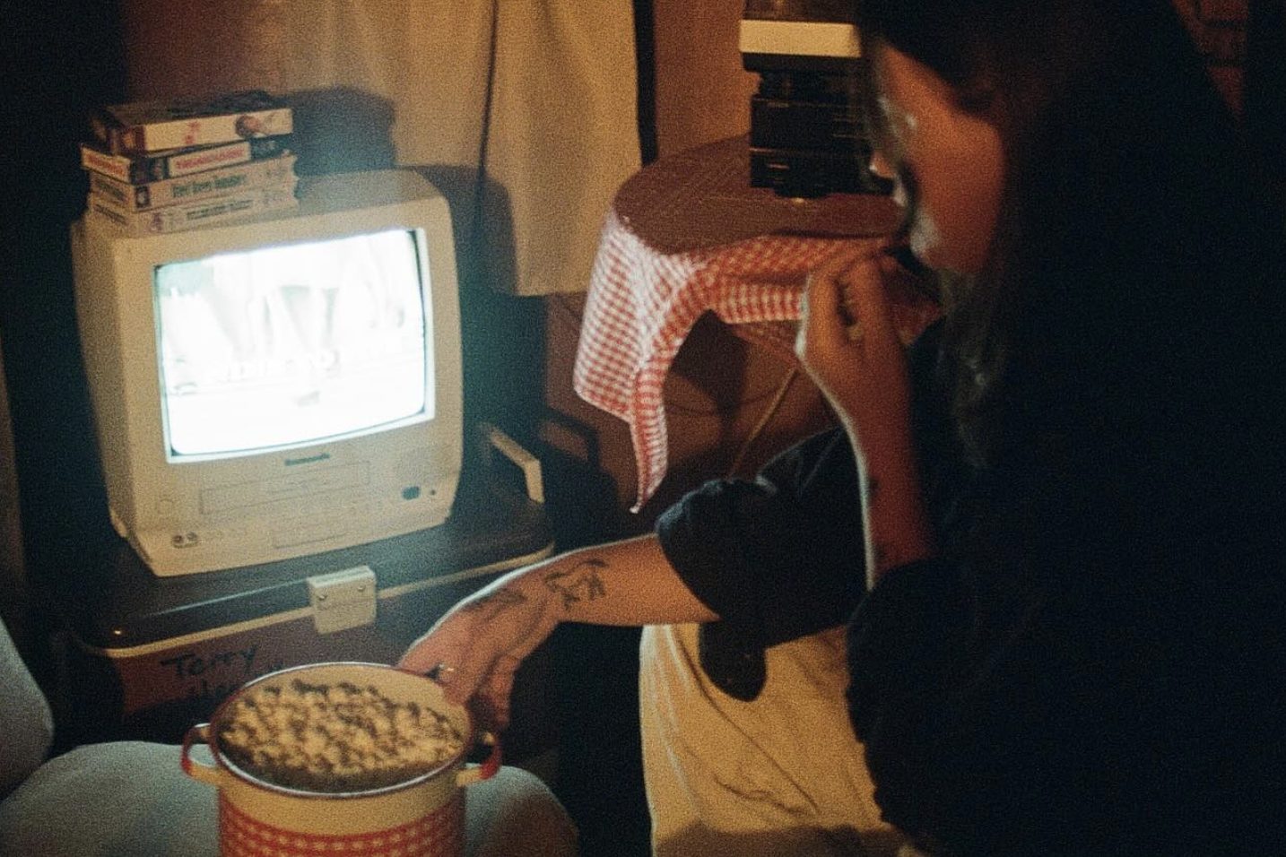 Person eating popcorn while watching a VHS tape glow on an old television at night