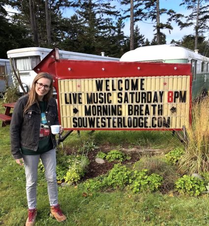 Woman standing beside a red marquee sign reading Welcome Live Music Saturday 8pm Morning Breath