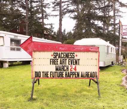 A red sandwich board sign reading Spaceness free art event March 2-4, did the future happen already, beside parked trailers