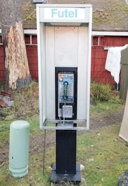A Futel branded payphone booth standing on grass in front of a red barn wall