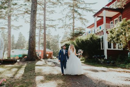 Bride and groom walk hand in hand up a sunlit path toward the red Sou'wester lodge building