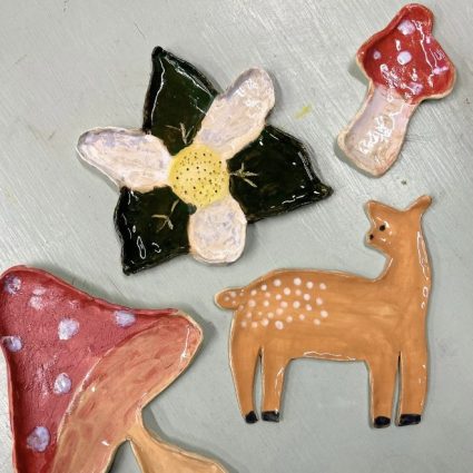 Painted clay charms shaped like a flower, red spotted mushrooms and a deer