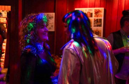 Two women dance together indoors under colorful disco lights