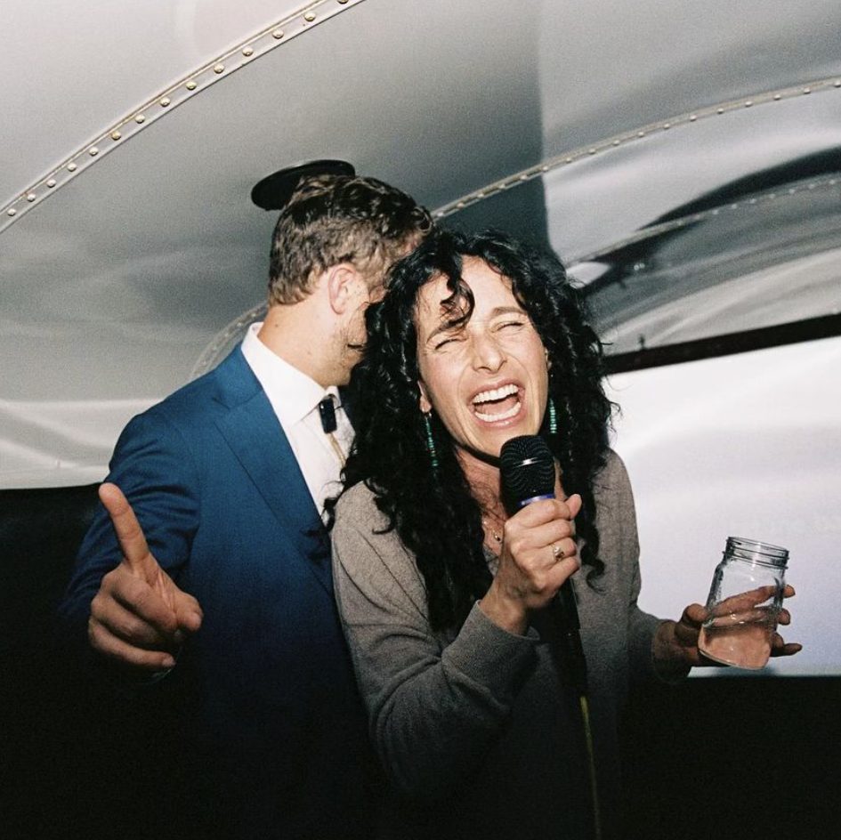 Man in a suit and woman with curly hair singing into a microphone inside the karaoke bus