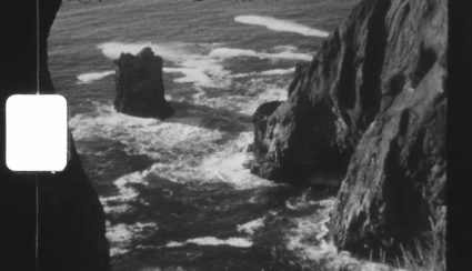 Black and white film still of rocky sea stacks with waves breaking against the cliffs