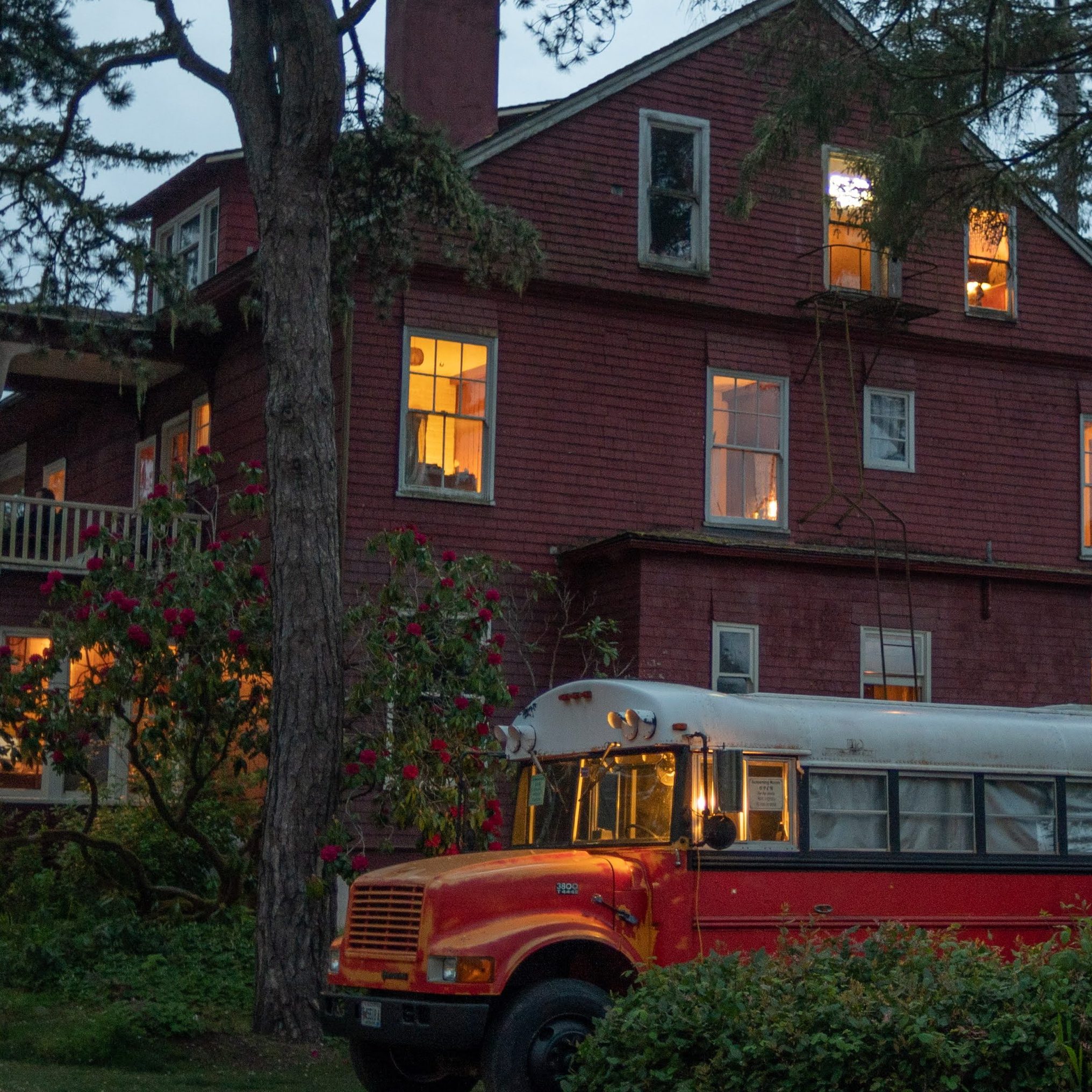 The Sou'wester Lodge glowing at dusk among tall pines with the red bus theater parked out front